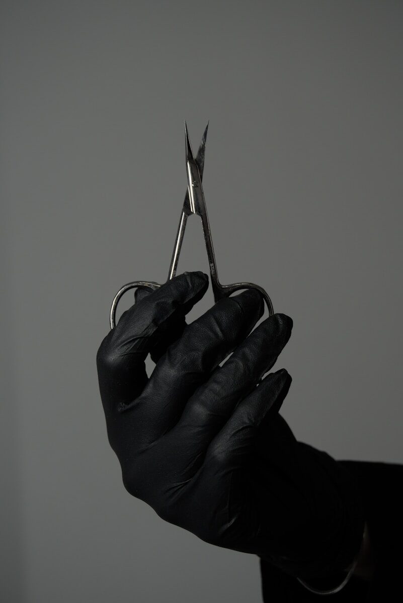 A person in black gloves holding a pair of scissors
